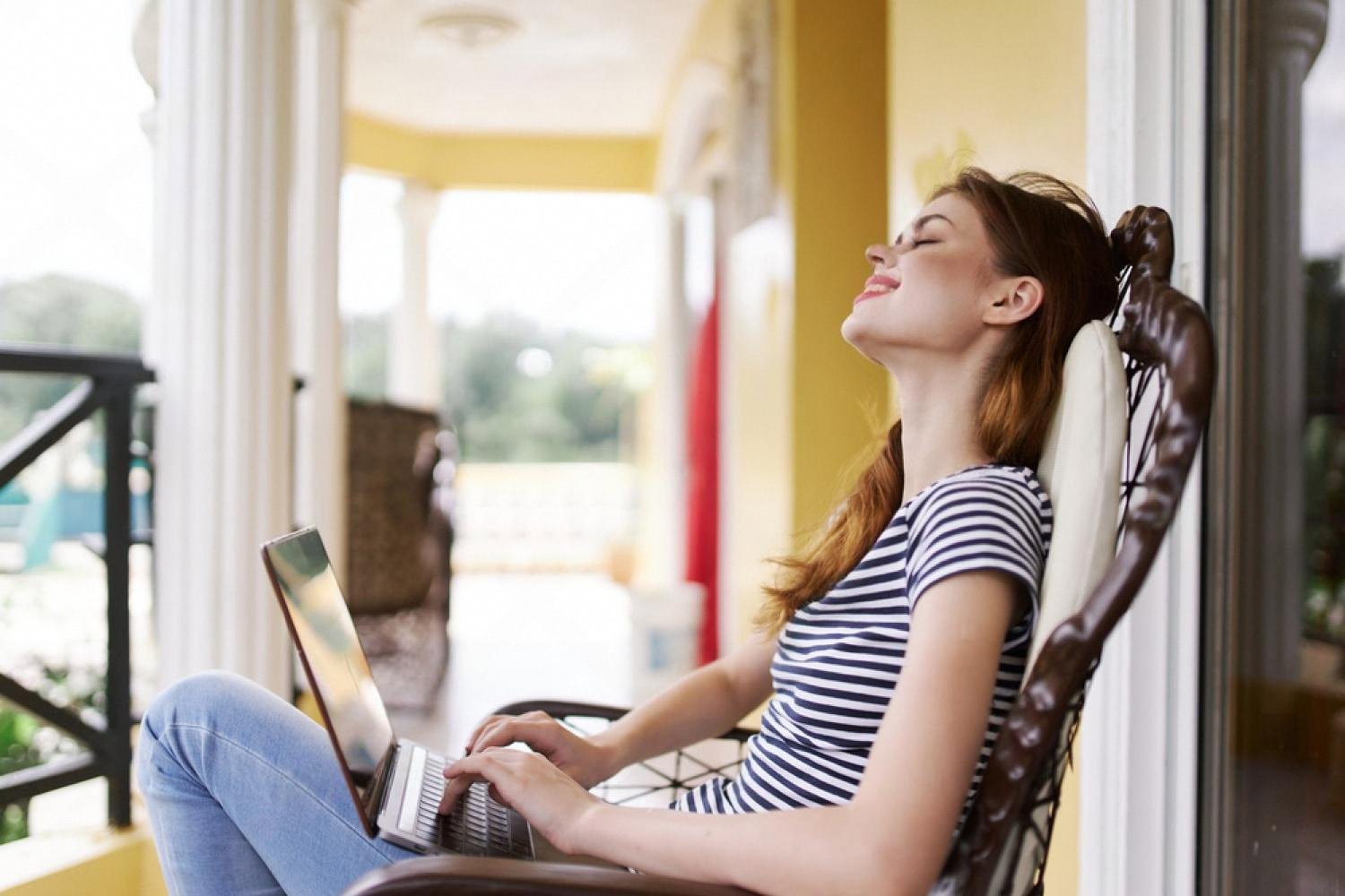 Relaxed hotel guest completing online registration on a laptop from her room balcony